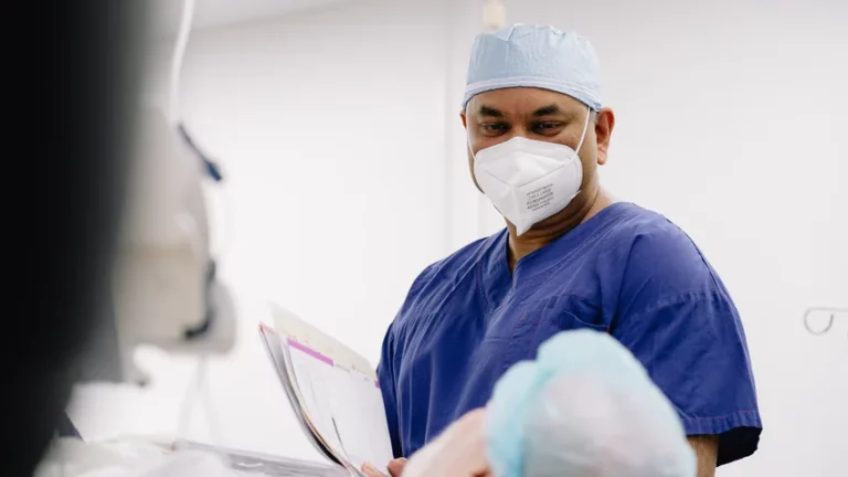 Orthopaedic surgeon in mask and blue scrubs reviewing patient chart