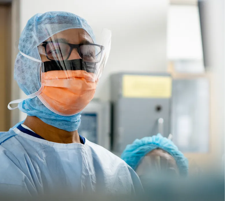 Surgeon in operating theatre wearing surgical cap, face mask, protective glasses and face shield