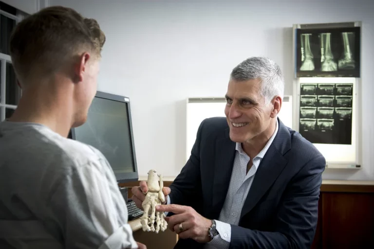 Orthopaedic surgeon explaining foot structure using anatomical model to young male patient during clinical assessment