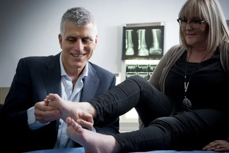 Podiatric specialist examining female patient's foot and ankle mobility during clinical assessment with foot X-rays displayed in background