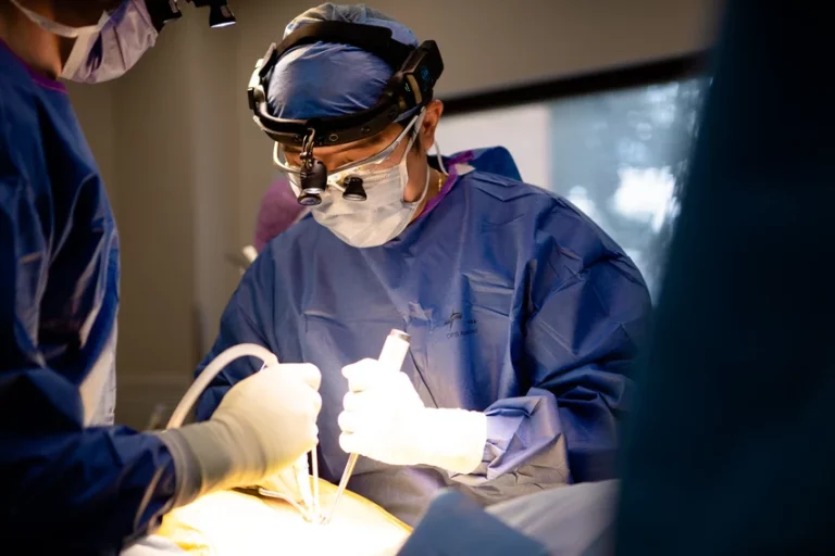 Orthopaedic surgeon performing a procedure in operating theatre, wearing surgical loupes and blue scrubs