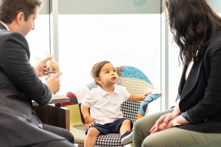 Paediatric orthopaedic consultation with young child seated in colourful chair while specialist demonstrates anatomical joint model and explains treatment to parent