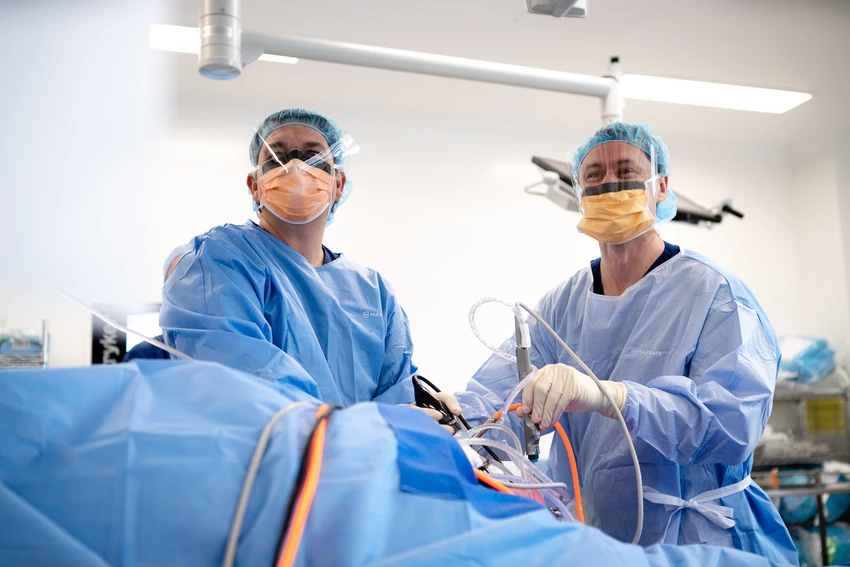 Healthcare professionals in sterile gowns and face shields performing surgical procedure in bright operating room