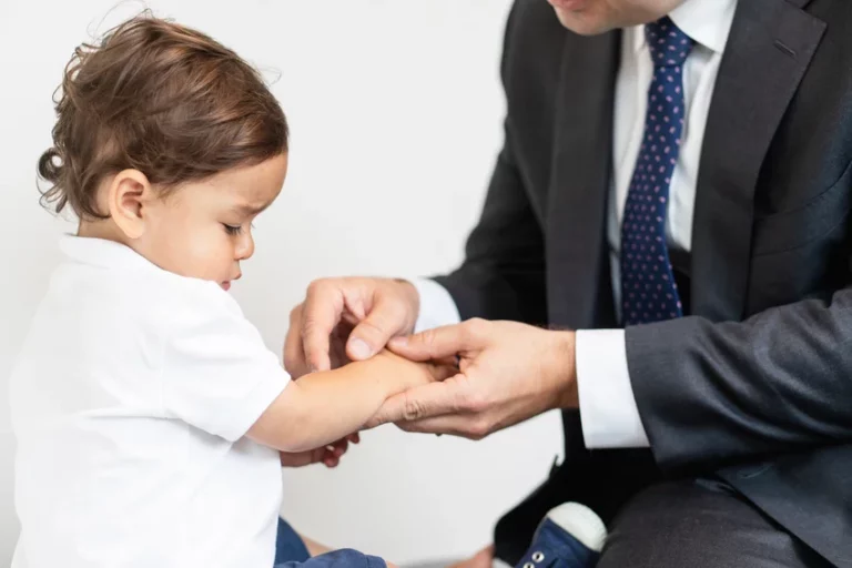 Orthopaedic specialist gently examining toddler's wrist and finger mobility during clinical assessment, providing attentive care in professional medical environment