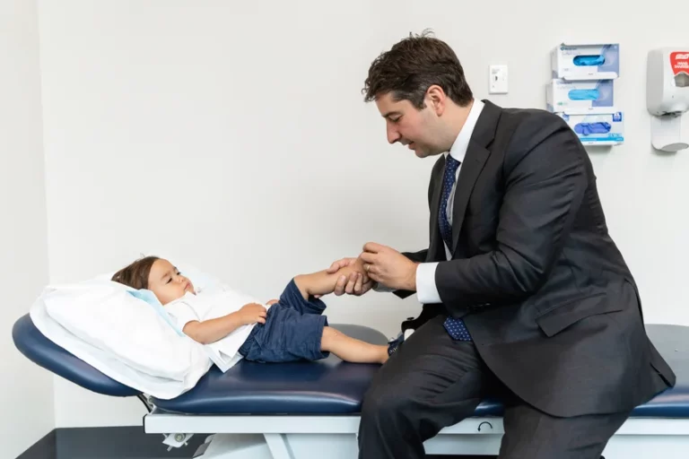 Paediatric orthopaedic specialist examining young patient's leg mobility during clinical assessment, with child resting on examination table in modern medical facility