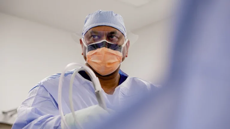 Surgeon in surgical attire with surgical cap, mask and face shield performing a procedure