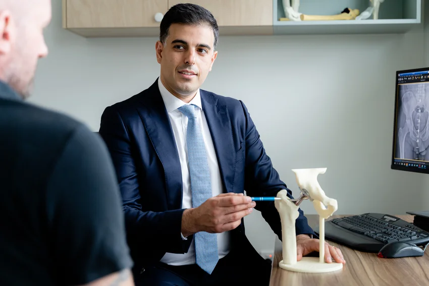 Orthopaedic surgeon in professional attire demonstrating hip joint model