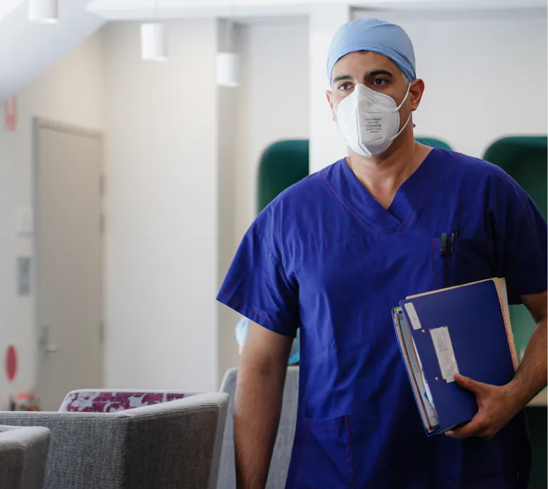 Orthopaedic surgeon in blue scrubs, surgical cap, and mask holding patient files