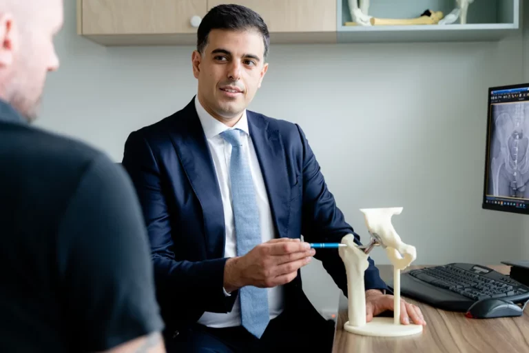 Orthopaedic surgeon in professional attire demonstrating hip joint model