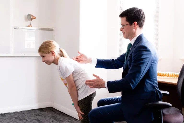 Orthopaedic specialist examining young patient's posture during spinal assessment