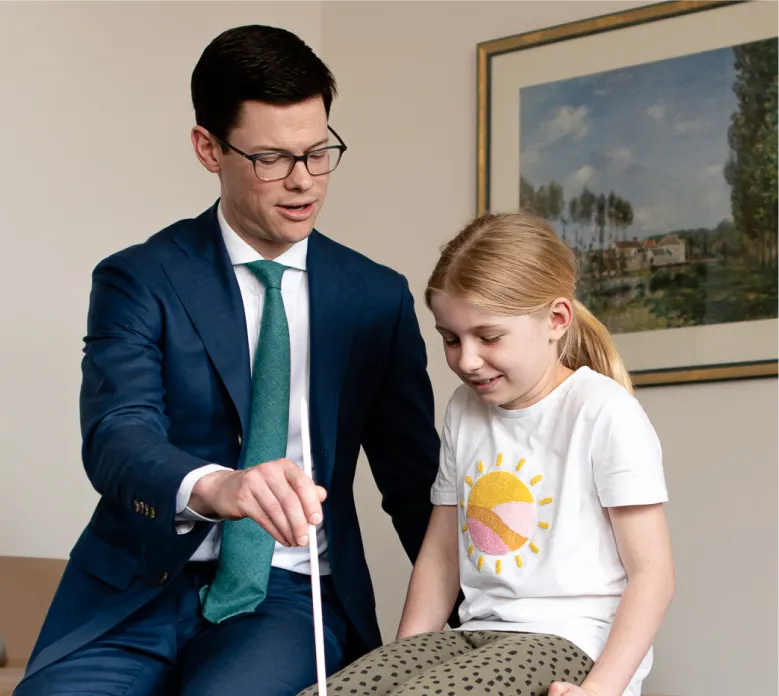 Paediatric orthopaedic specialist in navy suit examining young patient's knee during clinical consultation